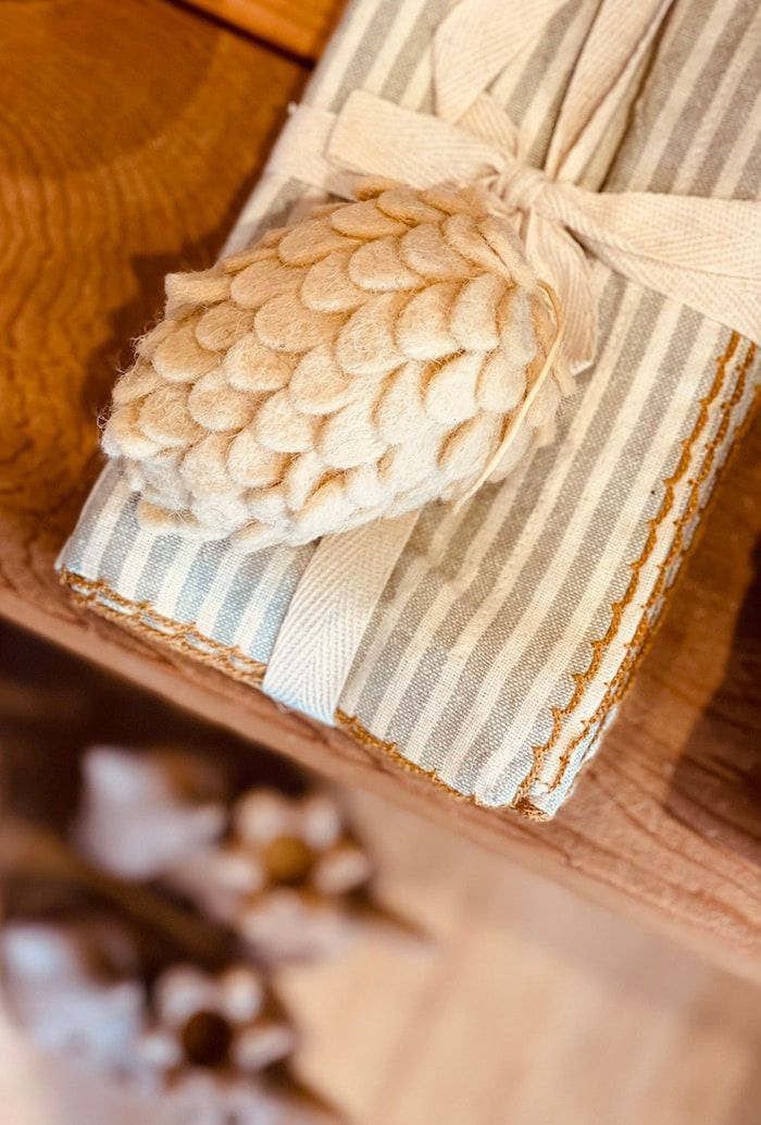 Beige pinecone napkin ring on a striped cream-and-blue cloth napkin beside a wooden table.