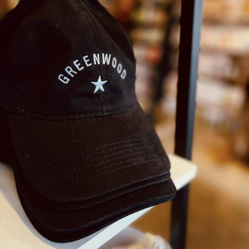 Black cap with “GREENWOOD” text and a white star logo on a shelf