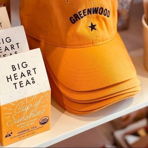 Orange “GREENWOOD” cap beside Big Heart Tea box on a shelf