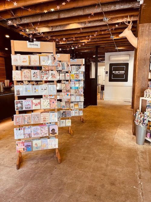 Greeting card display in a rustic shop, with rows of colorful cards on wooden racks and concrete floors.