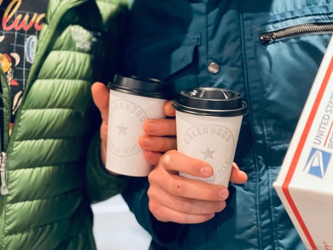 Two people holding white takeaway coffee cups in winter jackets near a café sign