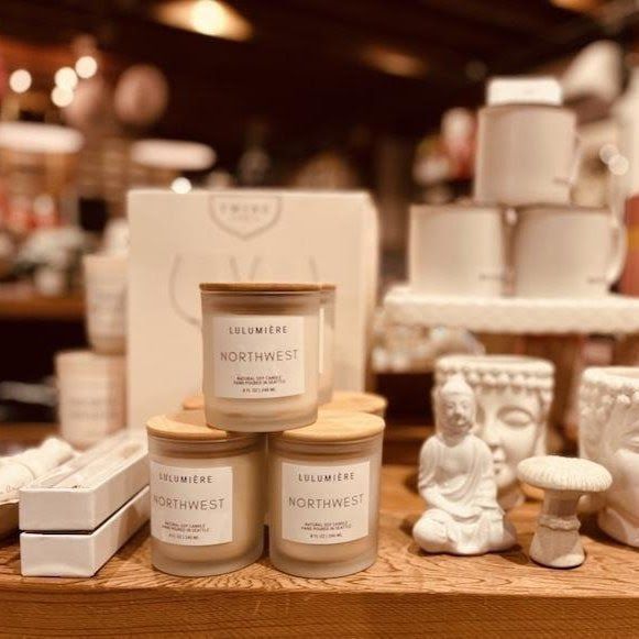 Candles and decorative items on a wooden display shelf in a warm, blurred shop setting