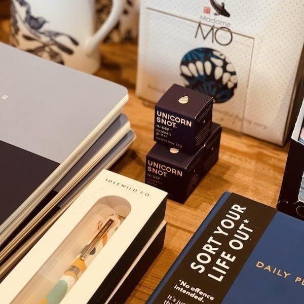 Desk display of boxed cosmetics and notebooks on a wooden table, including a black “Sorry for your life” book.