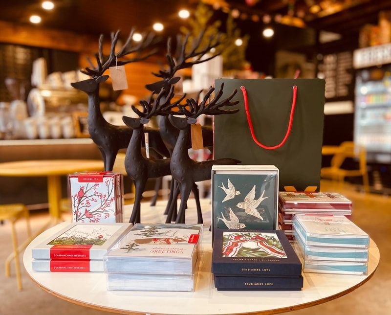 Gift display on a café table with cards, boxed items, black deer figurines, and a green shopping bag.