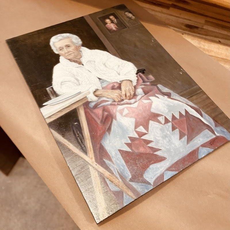 Portrait of an elderly person in a white blouse seated with a red-and-white quilt draped over their lap