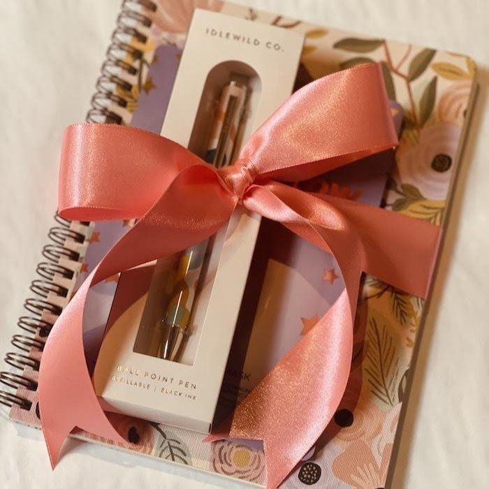 Gift set with coral ribbon, gold pen, and floral notebook on a spiral-bound planner