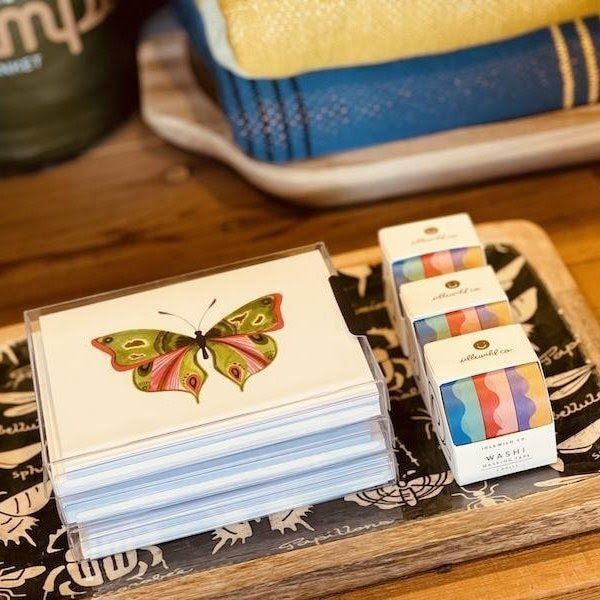 Butterfly-themed cards beside a small stack of colorful wrapped items on a wooden tray