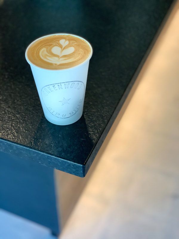 Small white to-go cup of latte art on a dark countertop near a blue wall.