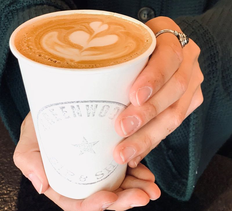 Hands holding a white cup of latte with heart-shaped foam art and a silver ring on one finger