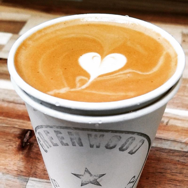 Latte in a white cup with heart-shaped foam art on a wooden table