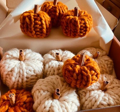 Assorted knitted pumpkin decorations in white and orange inside a cardboard box.