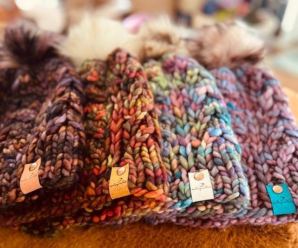 Colorful knitted hats with pom-poms arranged in a row on a fuzzy surface