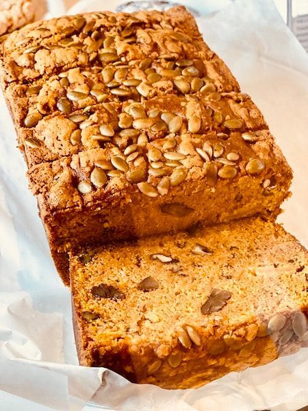 Loaf of nut-topped bread with one slice cut on parchment paper