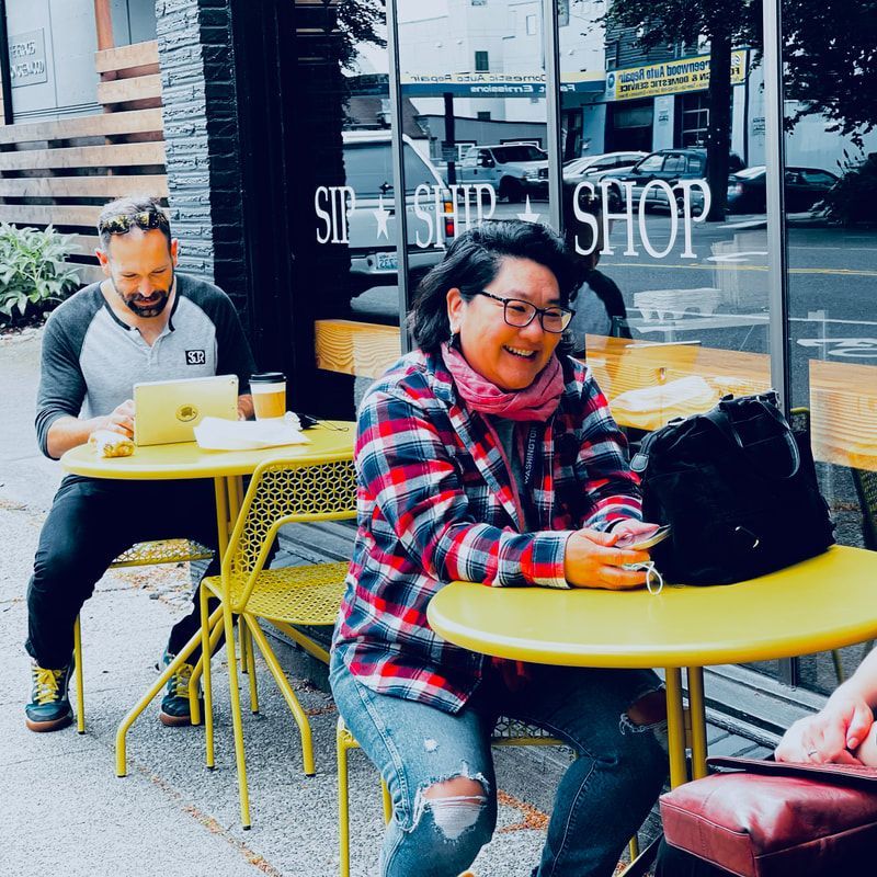 Two people smiling at yellow café tables outside a shop