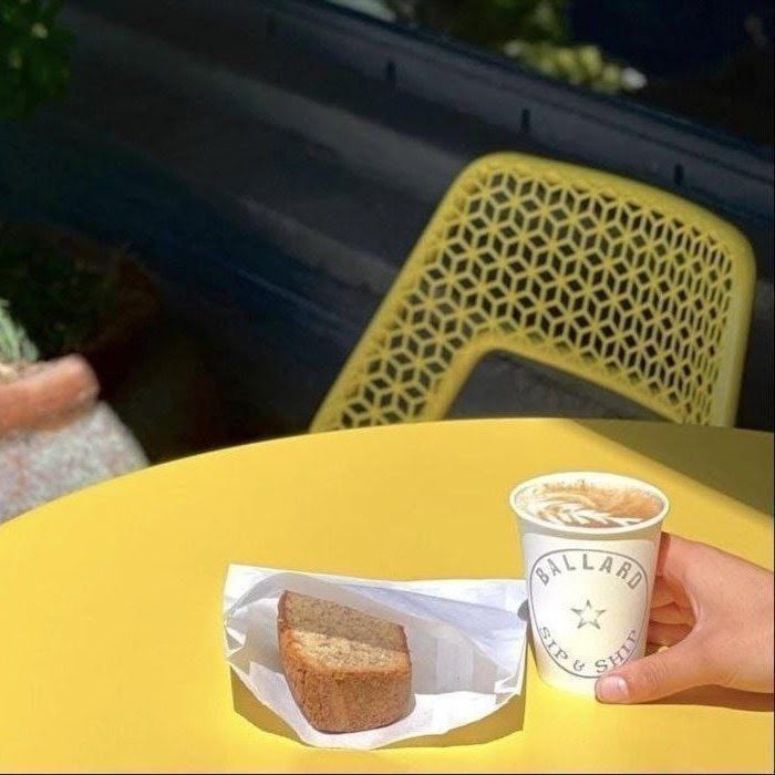 Yellow café table with a muffin on a napkin and a hand holding a coffee cup on a patio