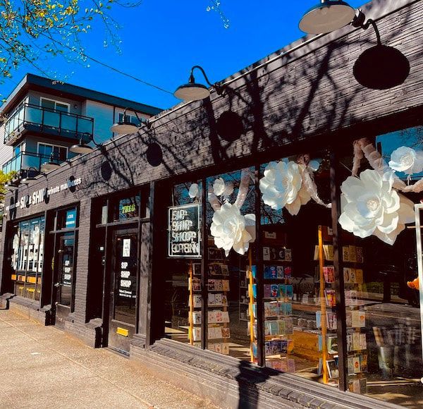 Sunlit storefront with dark wood facade, large windows, and white flower decorations on a city street