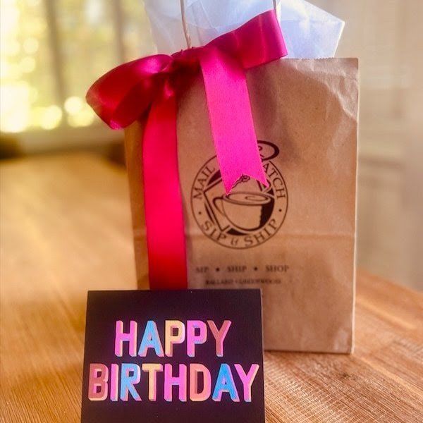 Gift bag with red ribbon and a “Happy Birthday” card on a warm, sunlit table.