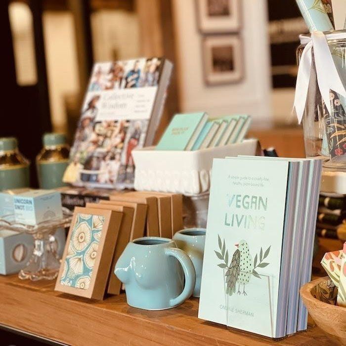 Display of vegan books and decor on a wooden table, including a mint mug and teapot.