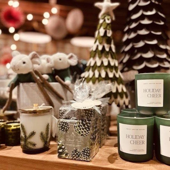 Holiday cheer candles and Christmas decor on a wooden display, including pine trees and silver gift boxes