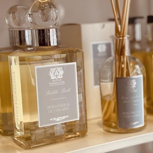 Glass reed diffuser bottles with gray labels on a shelf, one large square bottle and one small round bottle