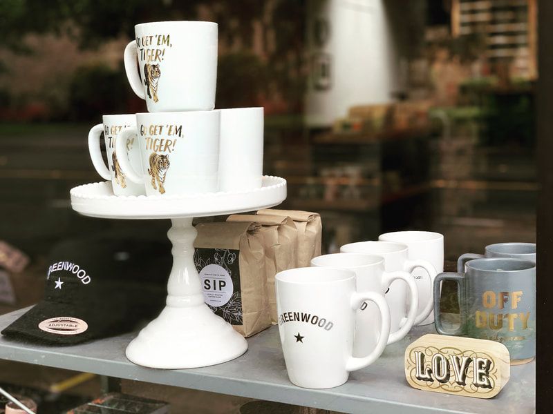 Coffee mugs and decorative signs displayed on a table outdoors with a blurred patio background