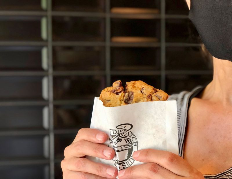 Person holding a white paper bag with pastries in front of a café counter