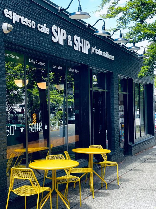 Yellow tables outside Sip & Ship café with black storefront and greenery above.