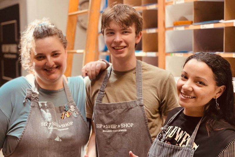 Three smiling aprons-clad workers standing together in a bakery or shop interior