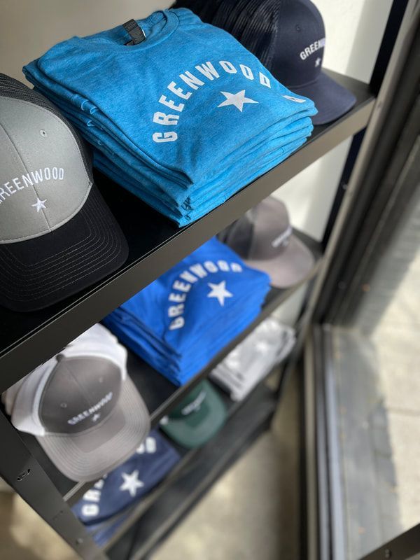 Stacked green and blue Greenhood T-shirts displayed on store shelves next to black caps