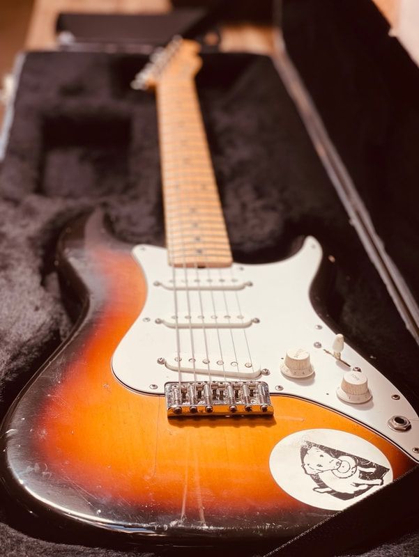 Sunburst electric guitar in an open case, with white pickguard and stickers on the body.