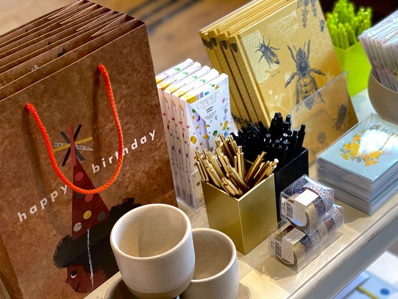 Stationery display with gift bags, cups, pencils, and cards on a bright shelf.