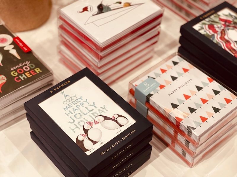 Stacked greeting cards and notebooks with colorful geometric and holiday-themed covers on a table