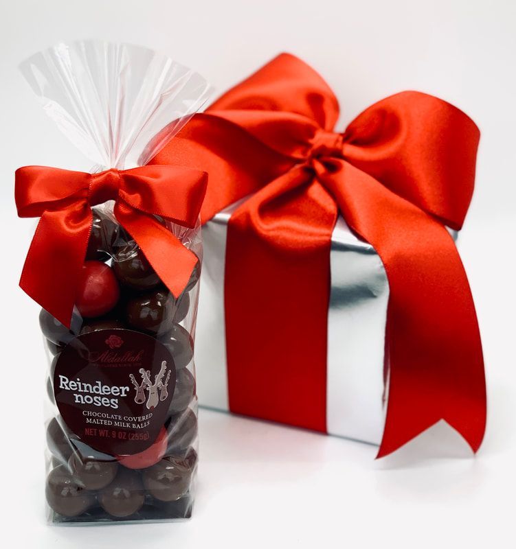 Red gift bag of Reindeer Moss chocolates beside a white box wrapped with a red satin ribbon