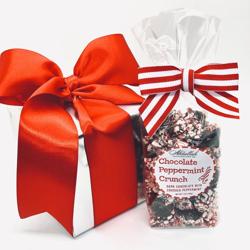 Red gift box with satin bow beside a clear bag of chocolate peppermint crunch tied with red-striped ribbon