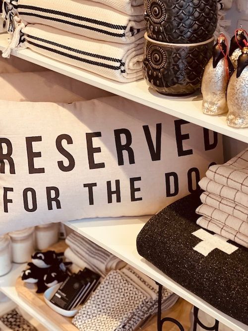 Stylish shelf with folded textiles and decor, featuring a “RESERVED FOR THE DOG” sign.