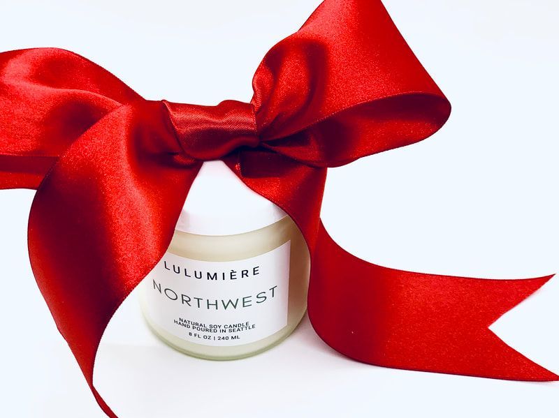 White candle jar wrapped in a large red satin bow on a white background