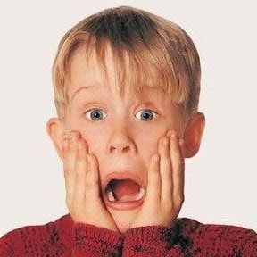 Shocked child with hands on cheeks, mouth open, wearing a red sweater on a plain background