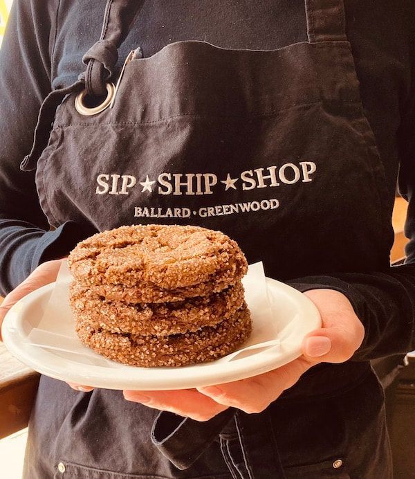 Hands holding a plate with a stacked cinnamon pastry in front of a Sip + Ship + Shop apron