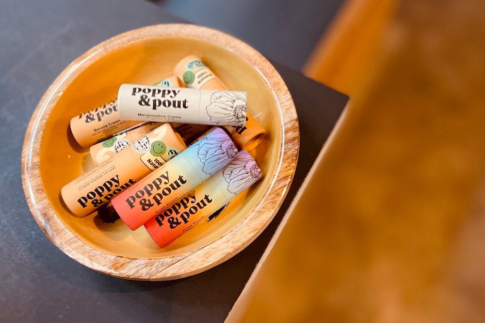 Wooden bowl holding several colorful lip balm tubes on a dark table