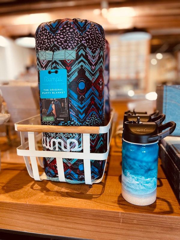 Blue-and-brown patterned tumbler in a white rack beside a blue ombré bottle on a wooden counter