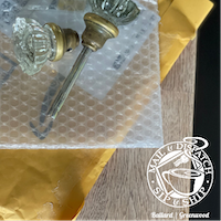 Vintage glass drawer pulls in bubble wrap inside a gold mailer box with a shop logo.