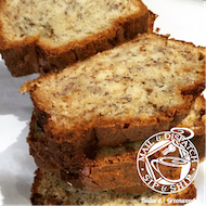 Two slices of banana bread on a white plate, golden-brown with a crumbly top and visible banana pieces