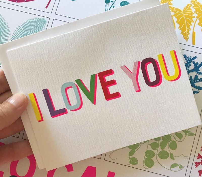 Hand holding a white card with colorful raised text reading “I LOVE YOU”