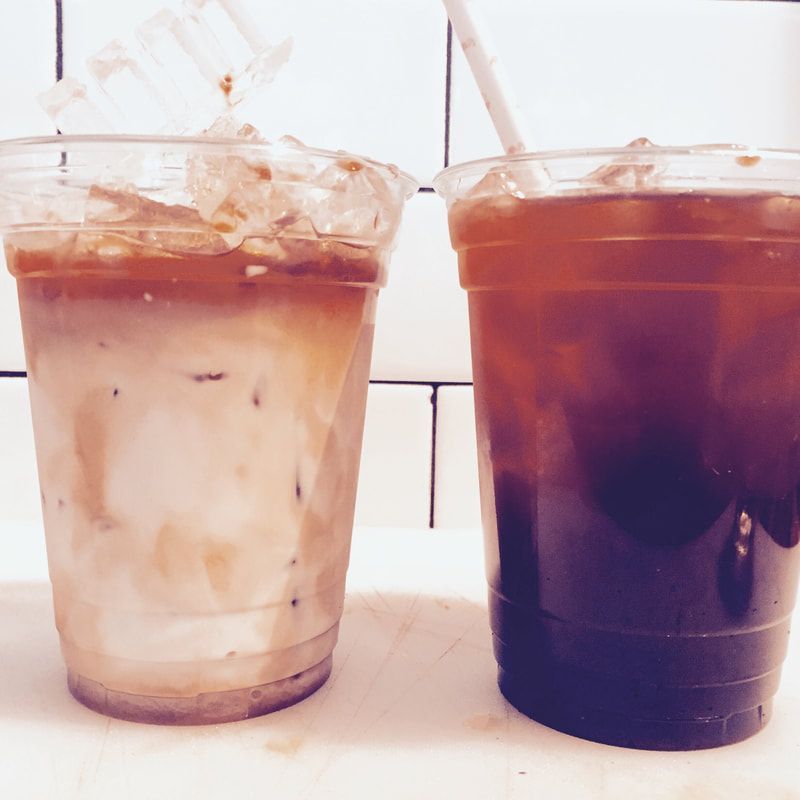 Two iced drinks in clear plastic cups on a table, one light brown and one dark brown.