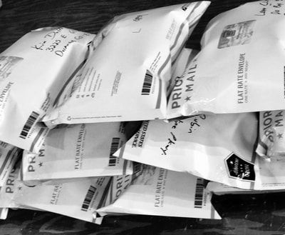 Stack of white padded mail envelopes piled in a bin, with barcodes and shipping labels visible