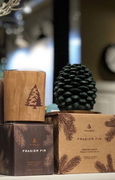 Rustic pine-scented candles and packaging with pinecone accents on a blurred indoor table