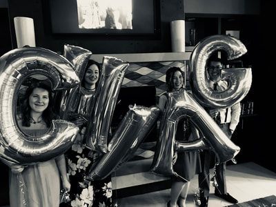 People holding large metallic balloon letters spelling “CHEER” in a dark indoor setting