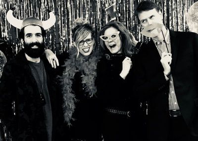 Four people posing together at a party, smiling in costume against a shiny backdrop.