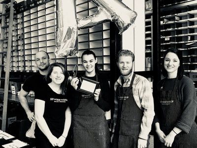 Five people in work aprons standing in a warehouse, holding a plaque and smiling at the camera.