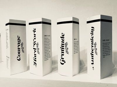 Four white cosmetic cartons with black accents and script labels standing in a row on a light surface.
